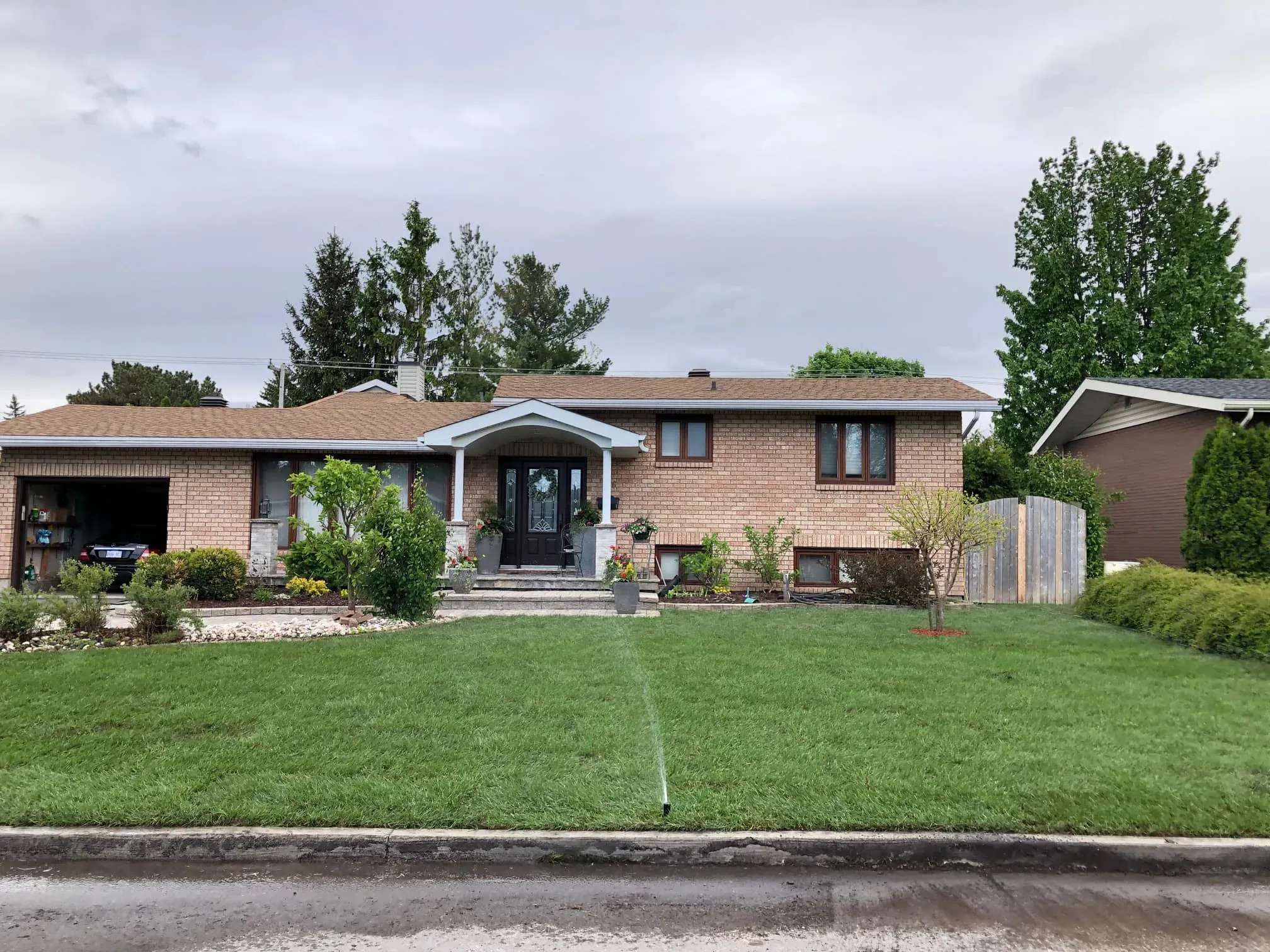 Freshly installed sod lawn being watered in front of a brick split-level home