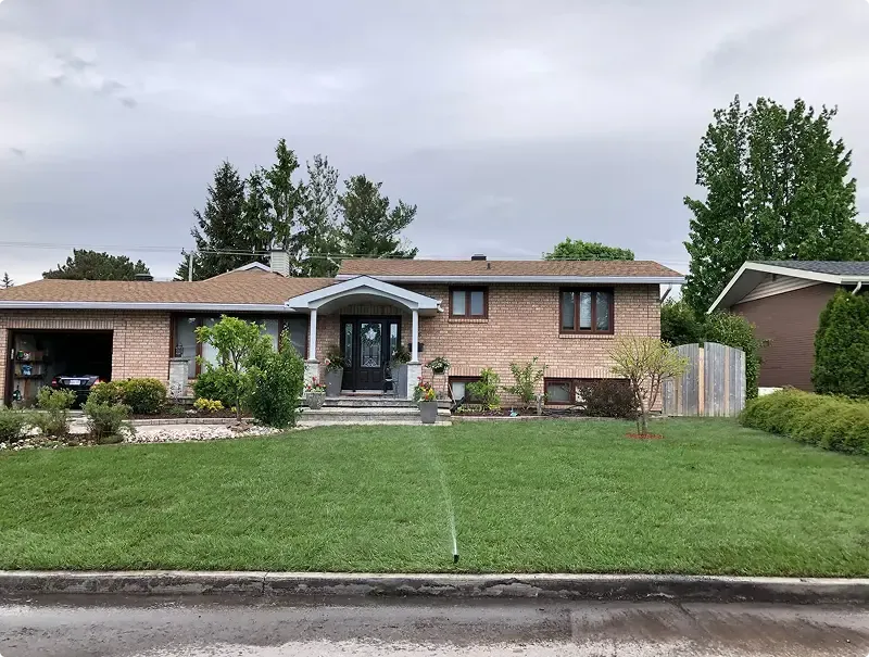 Freshly installed sod lawn being watered in front of a brick split-level Toronto home