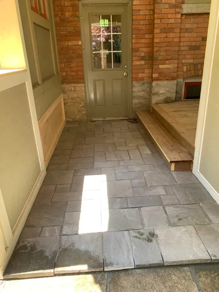 Interlocking pavers installed as a breezeway landing beside a brick wall and cedar deck step