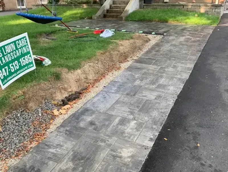 New interlock paver walkway along a driveway with the JJ's job sign on the lawn