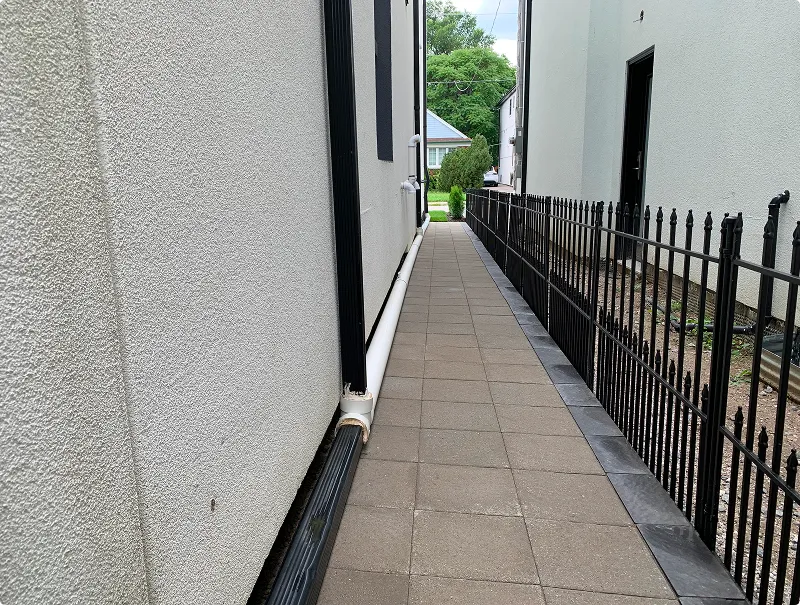 Tan paver path with charcoal border running along a narrow side yard