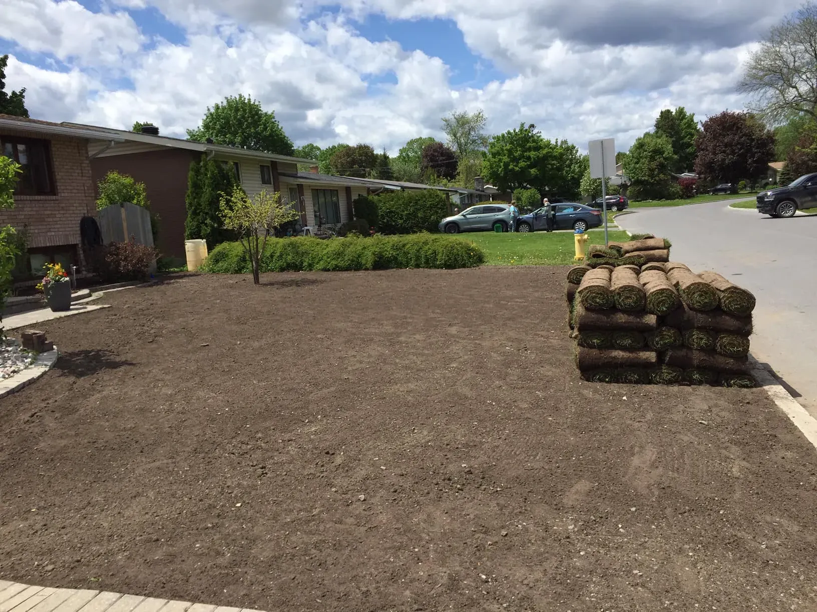 Rolls of fresh sod stacked beside a graded front yard ready for installation