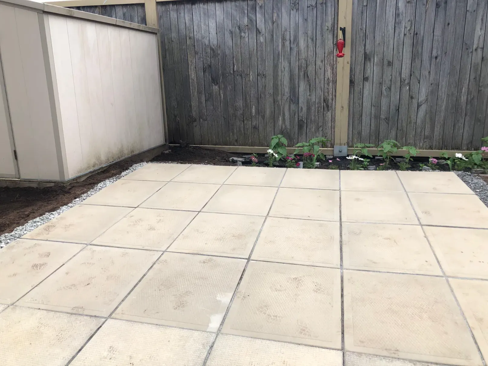 Newly laid square patio slabs with a fresh planting bed along the fence