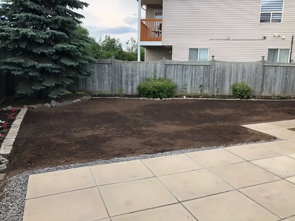 Backyard graded with fresh topsoil beside a new slab patio and brick garden edging